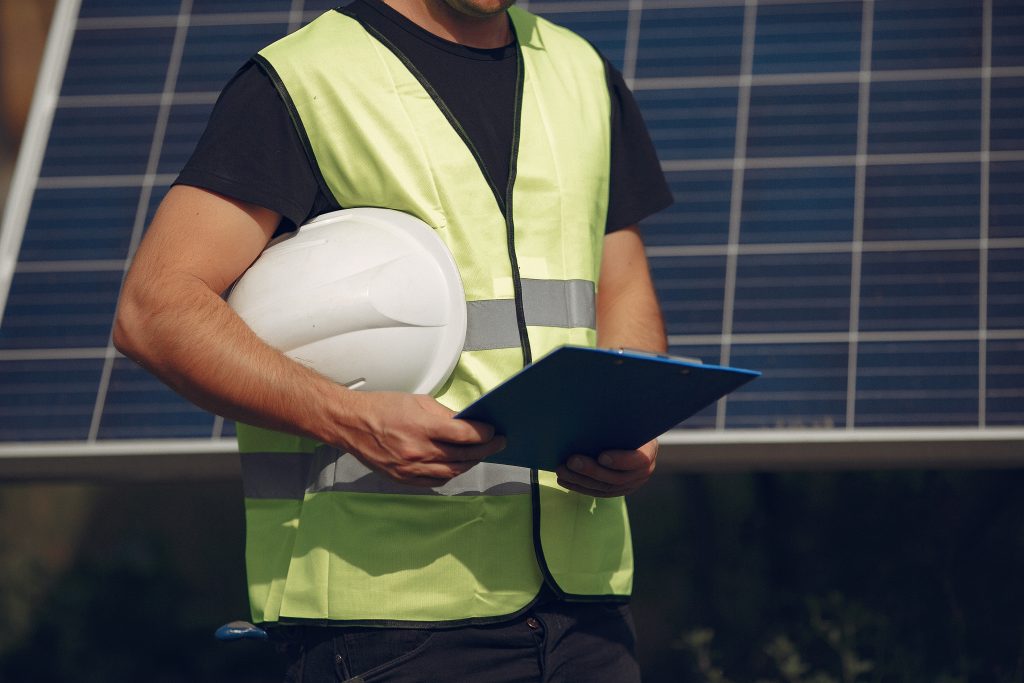 Engineer in a white helmet. Man near solar panel. Worker with a folder.